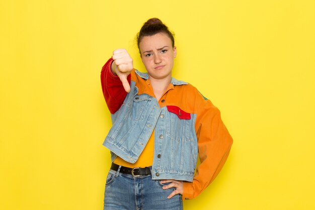 A front view young female in yellow shirt colorful jacket and blue jeans posing