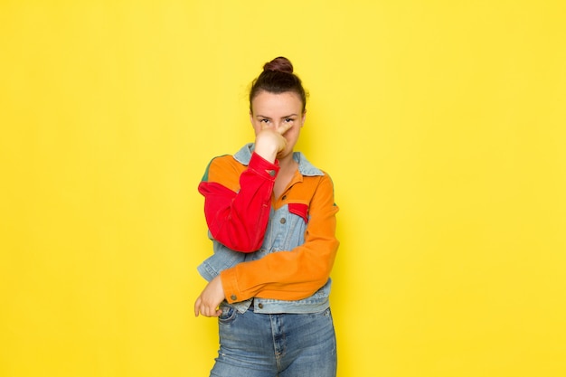 A front view young female in yellow shirt colorful jacket and blue jeans posing