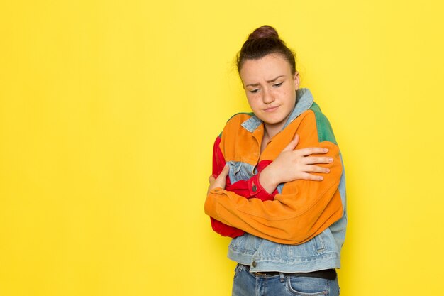 A front view young female in yellow shirt colorful jacket and blue jeans posing