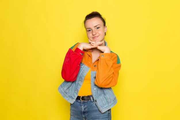 A front view young female in yellow shirt colorful jacket and blue jeans posing