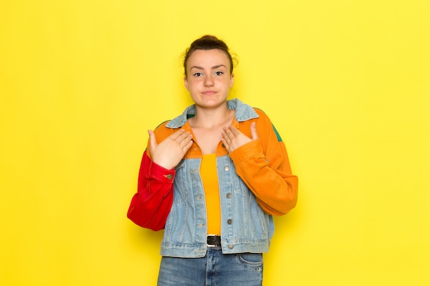 A front view young female in yellow shirt colorful jacket and blue jeans posing