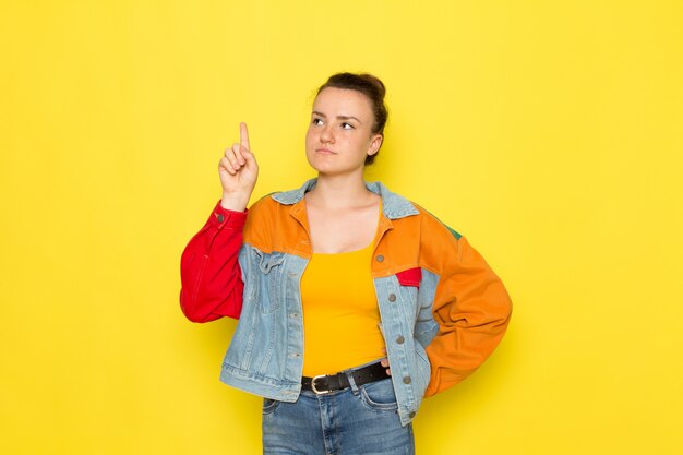 A front view young female in yellow shirt colorful jacket and blue jeans posing