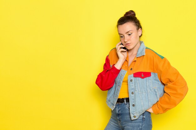 黄色のシャツのカラフルなジャケットとブルージーンズが電話で話している正面の若い女性