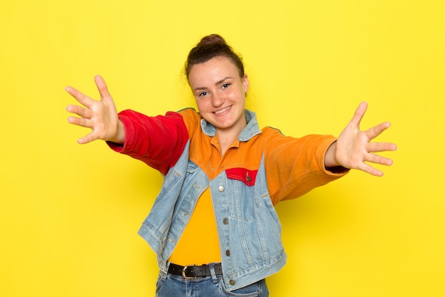 Foto gratuita una giovane donna vista frontale in giacca gialla camicia colorata e jeans blu con le braccia spalancate e sorridere uno il viso