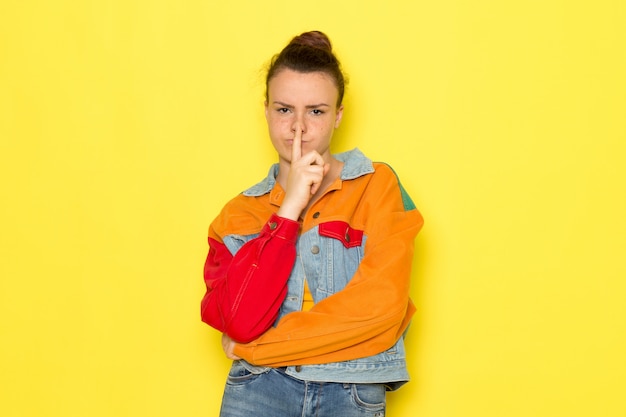 A front view young female in yellow shirt colorful jacket and blue jeans