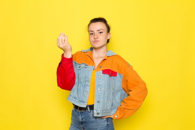 A front view young female in yellow shirt colorful jacket and blue jeans