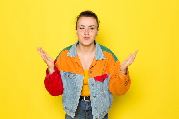 A front view young female in yellow shirt colorful jacket and blue jeans