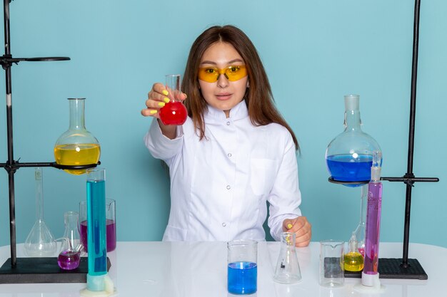 Front view of young feman chemist in white suit in front of table working with solutions