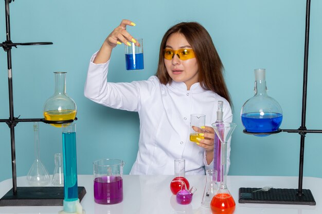 Front view of young feman chemist in white suit in front of table working with solutions