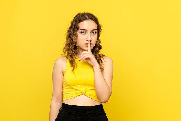 Front view of young girl asking to be quiet on yellow wall