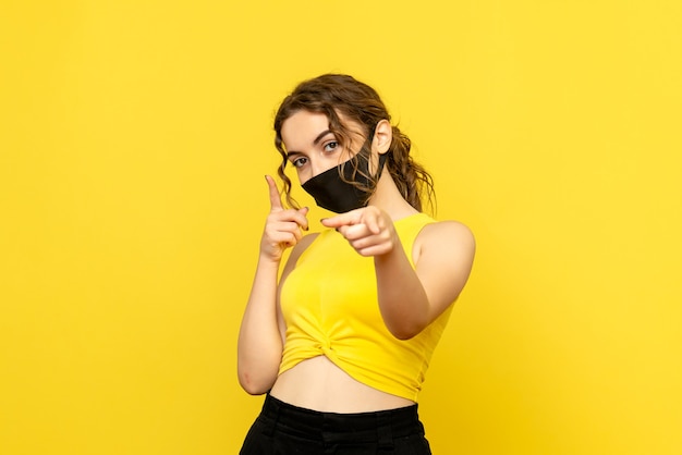 Front view of young girl in black mask on yellow wall