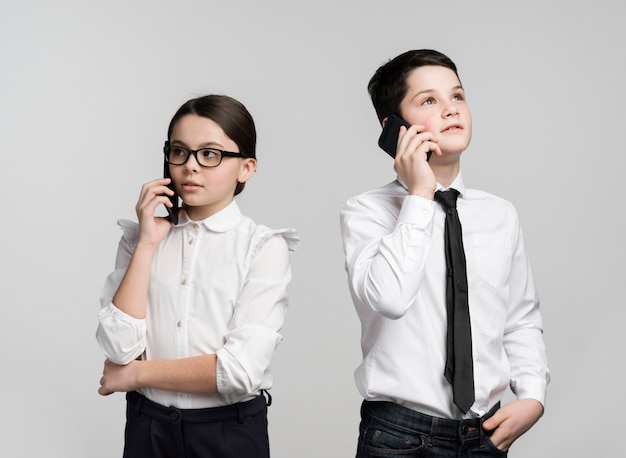 Front view young girl and boy talking on phones