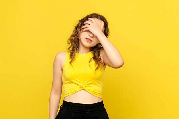 Front view of young girl covering her face on yellow wall