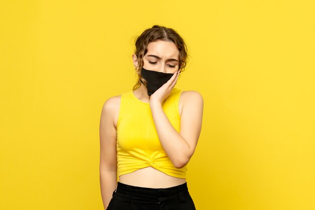 Front view of young girl having toothache on yellow wall