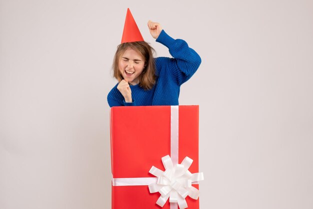 Front view of young girl inside red present box on the white wall