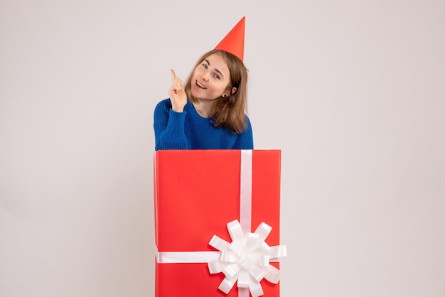 Front view of young girl inside red present box on the white wall