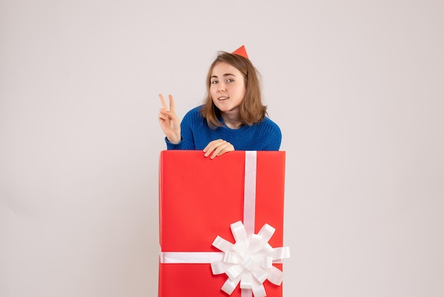 Front view of young girl inside red present box on the white wall