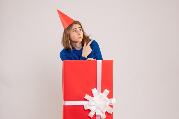 Front view of young girl inside red present box on the white wall