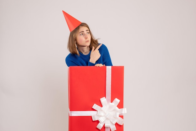 Front view of young girl inside red present box on the white wall