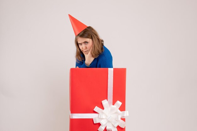 Вид спереди молодой девушки внутри красной подарочной коробки на белой стене
