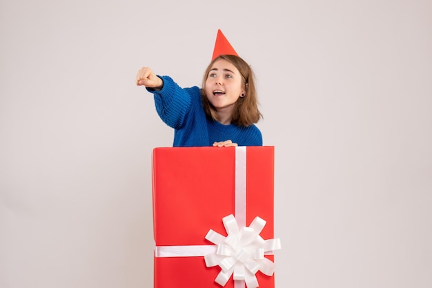 Вид спереди молодой девушки внутри красной подарочной коробки на белой стене