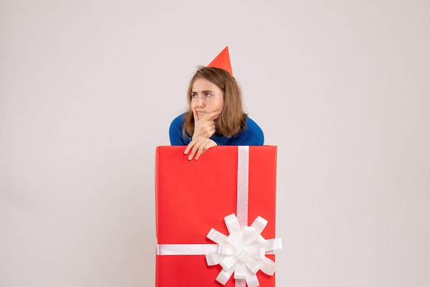 Front view of young girl inside red present box on white wall