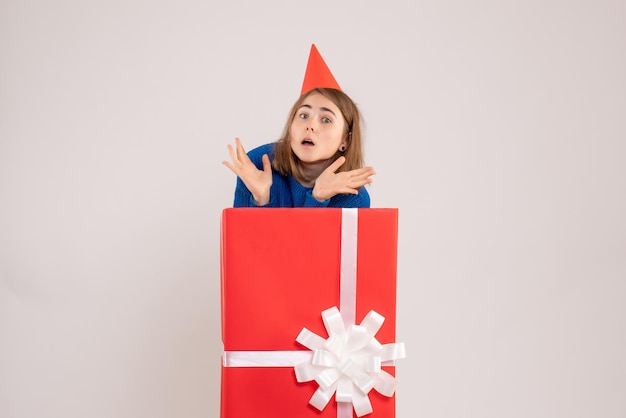 Front view of young girl inside red present box on white wall