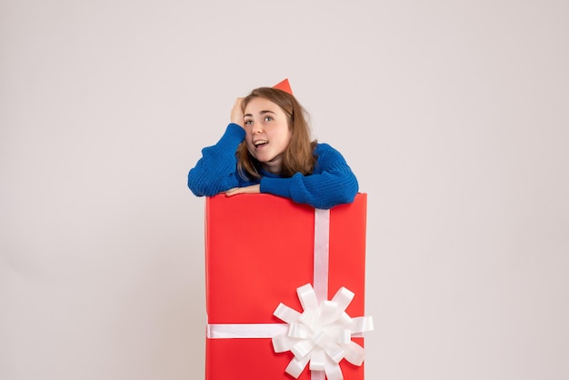 Front view of young girl inside red present box on white wall