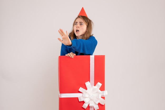 Front view of young girl inside red present box on white wall