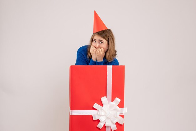 Front view of young girl inside red present box with scared face on white wall
