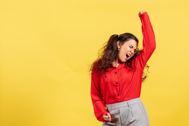 Front view young girl in red blouse with cute hair emotionally dancing on yellow background child color kid girl youth innocence