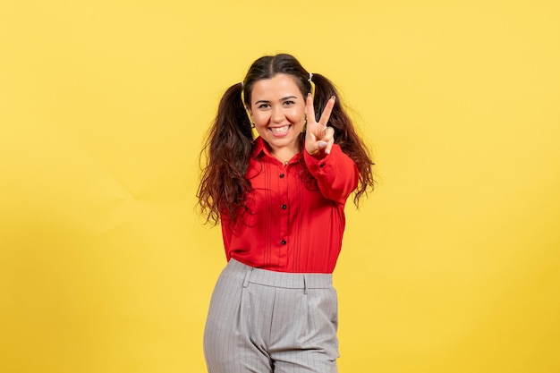 Front view young girl in red blouse with happy posing face on yellow background color innocence child youth kid girl