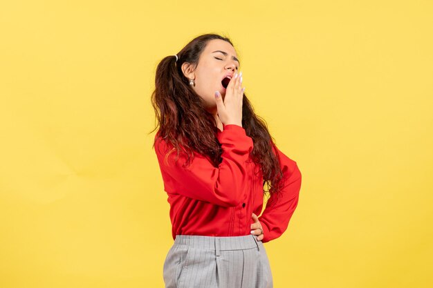 Front view young girl in red blouse yawning on yellow background female child kid girl youth emotion feeling