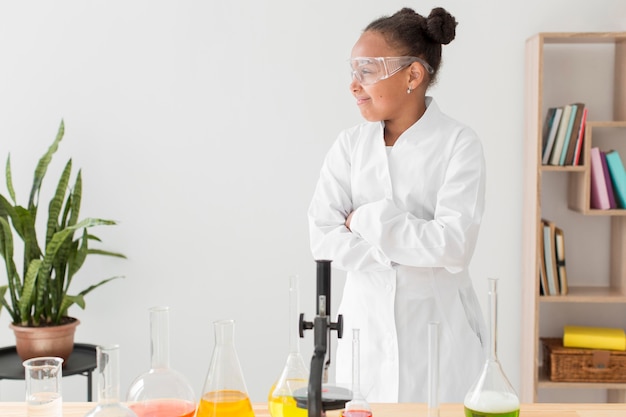 Front view of young girl scientist in lab coat with microscope and copy space