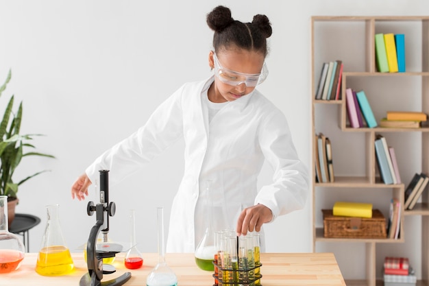 Front view of young girl scientist in lab coat with potions and microscope