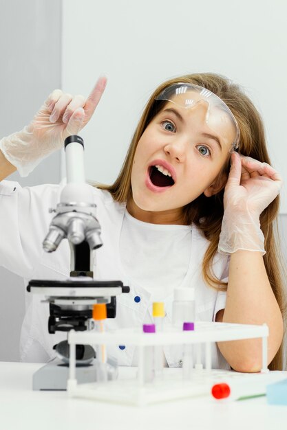 Вид спереди молодой девушки-ученого, использующей микроскоп и имеющей идею
