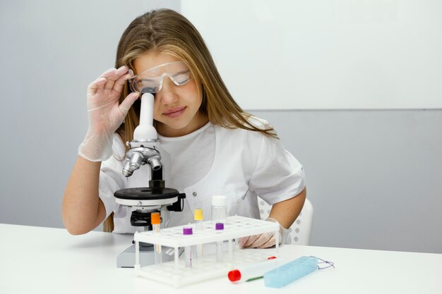 Front view of young girl scientist using microscope