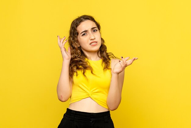 Front view of young girl with confused expression on yellow wall