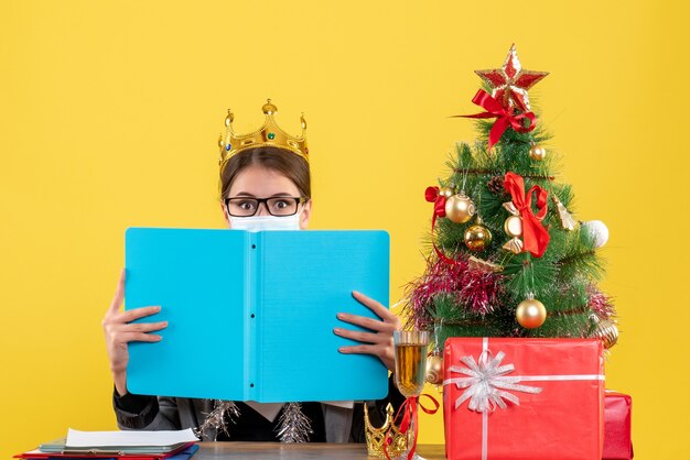 青い紙フォルダークリスマスツリーとギフトカクテルで彼女の顔を覆う王冠を持つ正面図の少女