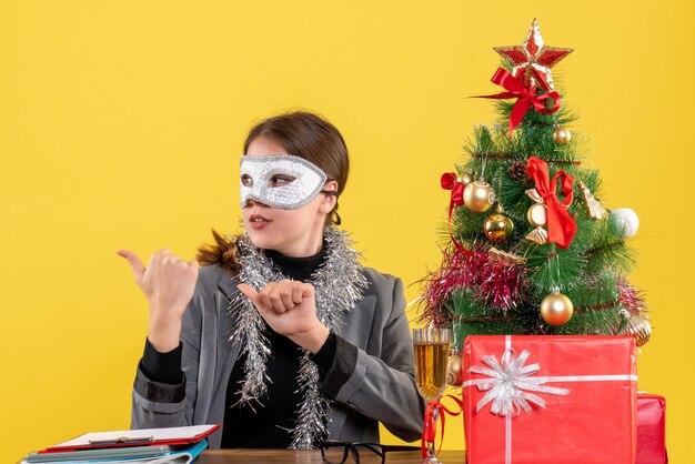 손가락 크리스마스 트리와 선물 칵테일 뭔가 보여주는 테이블에 앉아 마스크와 전면보기 어린 소녀