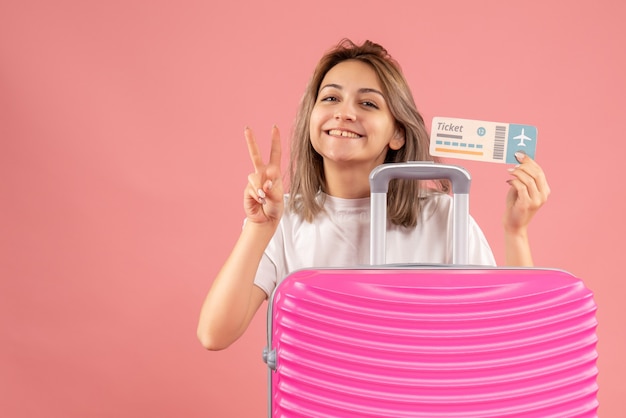 Front view young girl with pink suitcase holding ticket gesturing victory sign