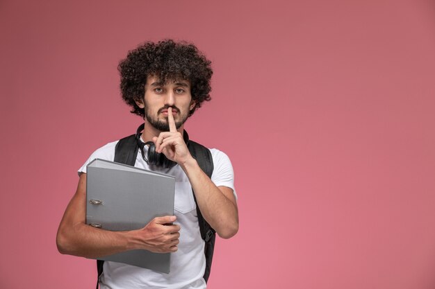 Front view young guy holding binder and showing keep silent gesture