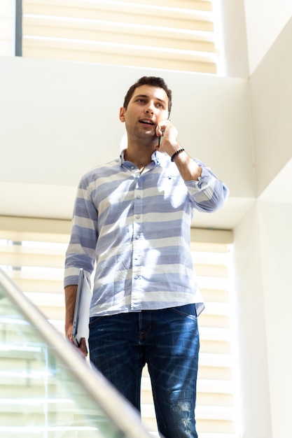 A front view young handsome man in striped shirt talking and discussing work issues on the phone during daytime work activity building