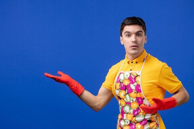 Front view of young housekeeper in apron standing on blue isolated wall