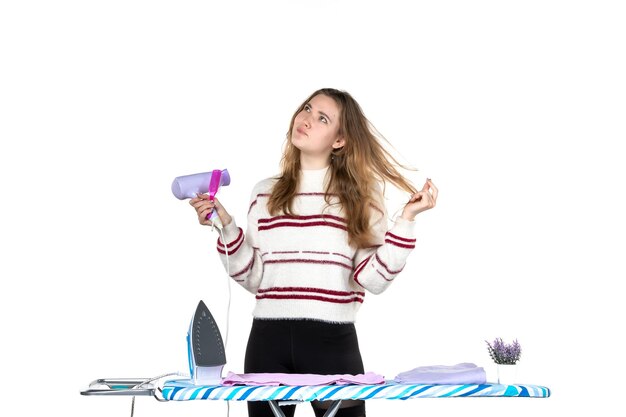 Front view young housewife holding brush and hairdryer on a white