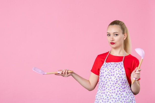 Бесплатное фото Вид спереди молодая домохозяйка держит столовые приборы на розовой стене
