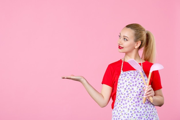 Front view young housewife  holding cutlery on pink wall