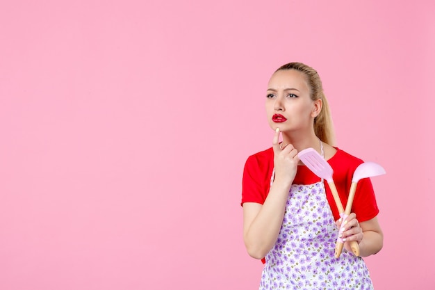 Front view young housewife  holding cutlery on pink wall