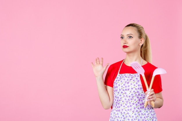 Free photo front view young housewife  holding cutlery on pink wall