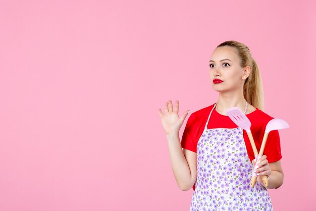 Front view young housewife  holding cutlery on pink wall
